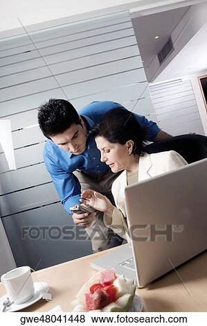 Stock Photo - Businesswoman sitting in front of a laptop with a businessman holding a mobile phone standing behind her. Fotosearch