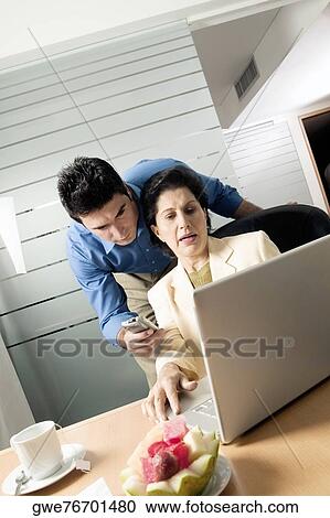 Businesswoman using a laptop with a businessman holding a mobile phone standing behind her View Large Photo Image Stock Image - Businesswoman using a laptop with a businessman holding a mobile phone standing behind her. Fotosearch