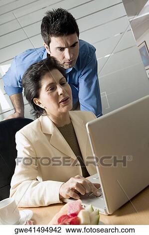 Businesswoman working on a laptop with another businessman standing behind her View Large Photo Image Stock Image - Businesswoman working on a laptop with another businessman standing behind her. Fotosearch