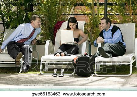 Businesswoman working on a laptop with two other businessmen looking at her View Large Photo Image Stock Image - Businesswoman working on a laptop with two other businessmen looking at her. Fotosearch