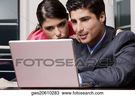 Stock Image - Close-up of a businessman and a businesswoman using a laptop. Fotosearch