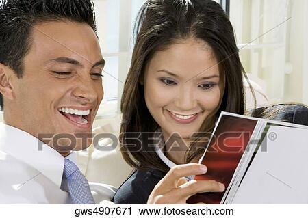Stock Image - Close-up of a businessman and a businesswoman reading a magazine. Fotosearch