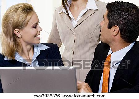 Close-up of a businessman and two businesswomen talking in front of a laptop View Large Photo Image Stock Photograph - Close-up of a businessman and two businesswomen talking in front of a laptop. Fotosearch
