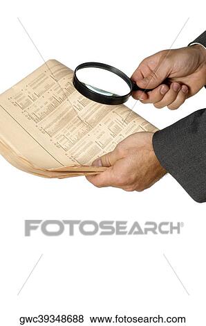 Stock Photo - Close-up of a businessman holding a magnifying glass over a newspaper. Fotosearch