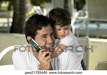Close-up of a father talking on a mobile phone with his son hugging from behind View Large Photo Image Stock Photo - Close-up of a father talking on a mobile phone with his son hugging from behind. Fotosearch