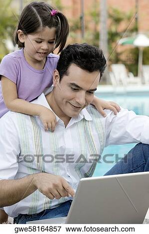 Stock Photo - Close-up of a father using a laptop with his daughter standing behind him. Fotosearch