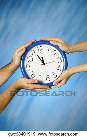 Stock Photo - Close-up of a man and a woman's hands holding a clock. Fotosearch