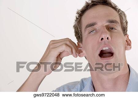 Stock Photo - Close-up of a mid adult man cleaning his ear with a cotton swab. Fotosearch
