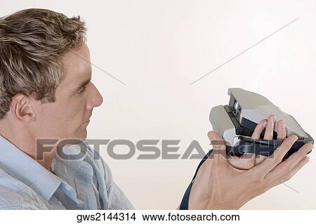 Picture - Close-up of a mid adult man holding an instant camera. Fotosearch