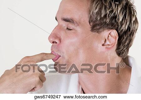 Stock Photo - Close-up of a mid adult man licking his finger. Fotosearch