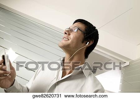 Stock Image - Close-up of a mid adult man listening to an MP3 Player. Fotosearch