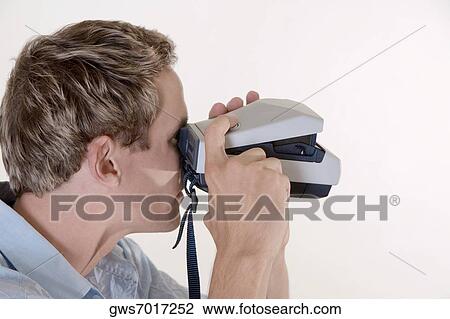 Stock Image - Close-up of a mid adult man looking through an instant camera. Fotosearch