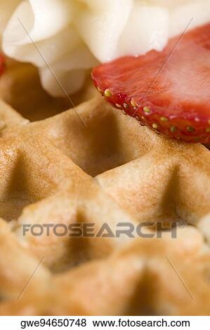 Stock Photo - Close-up of a waffle with whipped cream and strawberry slice on it. Fotosearch