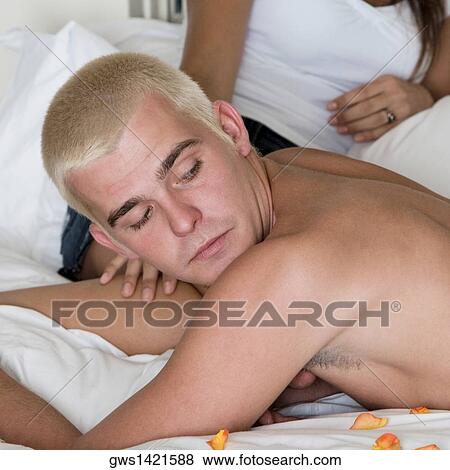 Close-up of a young man lying on the bed with a young woman sitting behind him View Large Photo Image Stock Photo - Close-up of a young man lying on the bed with a young woman sitting behind him. Fotosearch