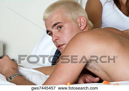 Close-up of a young man lying on the bed with a young woman sitting behind him View Large Photo Image Stock Photo - Close-up of a young man lying on the bed with a young woman sitting behind him. Fotosearch