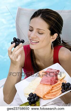 Stock Image - Close-up of a young woman eating fruits. Fotosearch