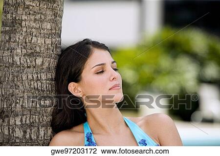 Close-up of a young woman leaning against a tree and thinking View Large Photo Image Stock Image - Close-up of a young woman leaning against a tree and thinking. Fotosearch