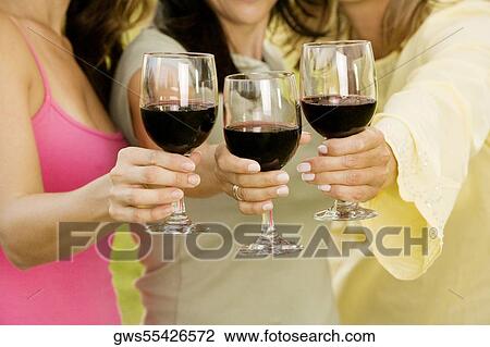 Stock Image - Close-up of three women holding glasses of red wine. Fotosearch