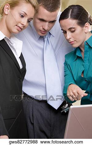 Close-up of two businesswomen and a businessman looking at a laptop View Large Photo Image Stock Photo - Close-up of two businesswomen and a businessman looking at a laptop. Fotosearch