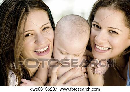Close-up of two young women holding a baby girl View Large Photo Image Stock Photo - Close-up of two young women holding a baby girl. Fotosearch