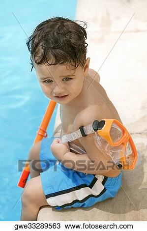Stock Image - High angle view of a boy holding snorkel sitting by the pool. Fotosearch