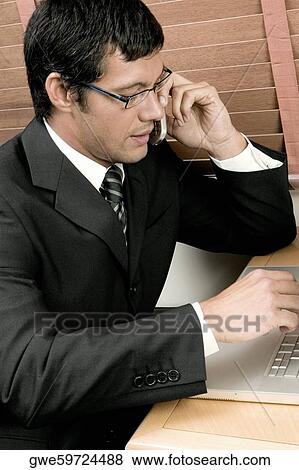 High angle view of a businessman sitting in front of a laptop using a mobile phone View Large Photo Image Stock Photo - High angle view of a businessman sitting in front of a laptop using a mobile phone. Fotosearch