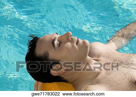 Stock Image - High angle view of a young man lying on a raft in a swimming pool. Fotosearch