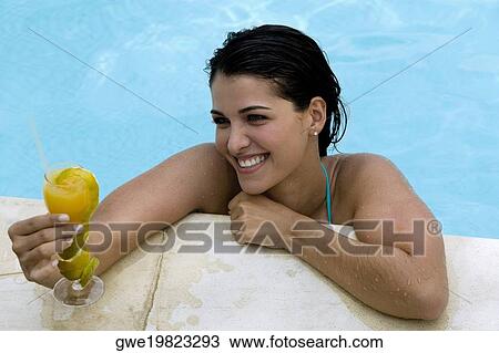 Stock Image - High angle view of a young woman holding a drink in a swimming pool. Fotosearch
