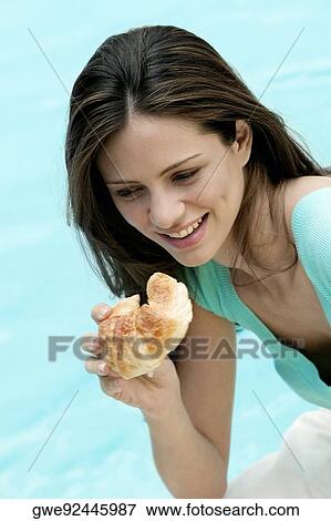 High angle view of a young woman holding a bun close to her mouth View Large Photo Image Stock Photo - High angle view of a young woman holding a bun close to her mouth. Fotosearch
