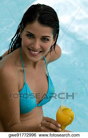 Stock Photograph - High angle view of a young woman holding a drink in a swimming pool. Fotosearch