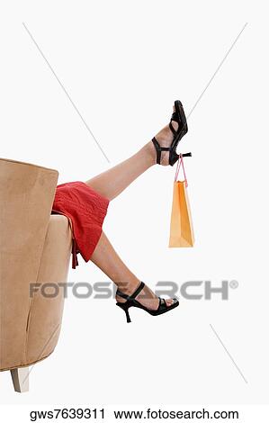 Stock Image - Low section view of a woman lifting a shopping bag with her heel. Fotosearch
