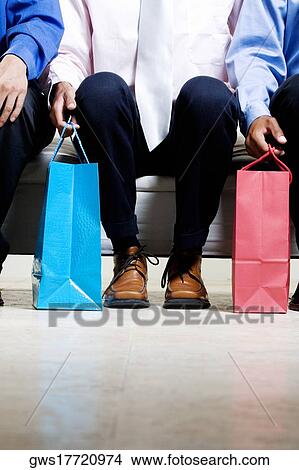 Low section view of three people sitting on a couch holding shopping bags View Large Photo Image Picture - Low section view of three people sitting on a couch holding shopping bags. Fotosearch