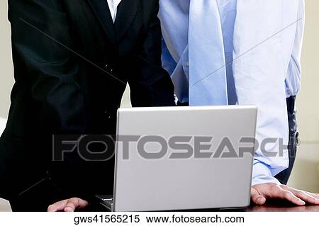 Stock Photography - Mid section view of a businessman and a businesswoman in front of a laptop. Fotosearch