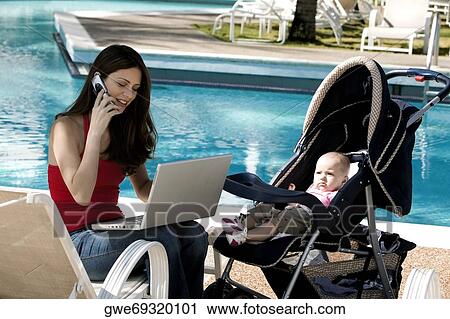 Mother talking on a mobile phone with her daughter beside her at the poolside View Large Photo Image Stock Image - Mother talking on a mobile phone with her daughter beside her at the poolside. Fotosearch