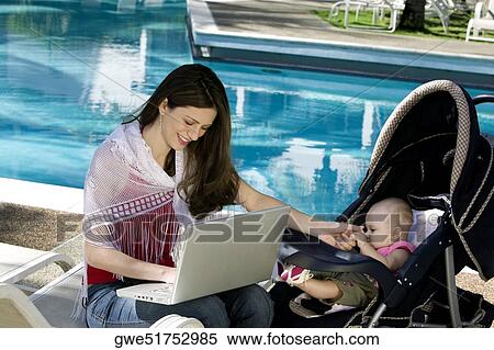 Mother using a laptop with her daughter beside her at the poolside View Large Photo Image Stock Photography - Mother using a laptop with her daughter beside her at the poolside. Fotosearch