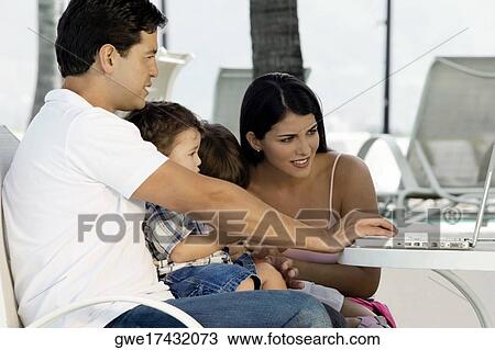 Parents with their two children sitting in front of a laptop View Large Photo Image Stock Image - Parents with their two children sitting in front of a laptop. Fotosearch