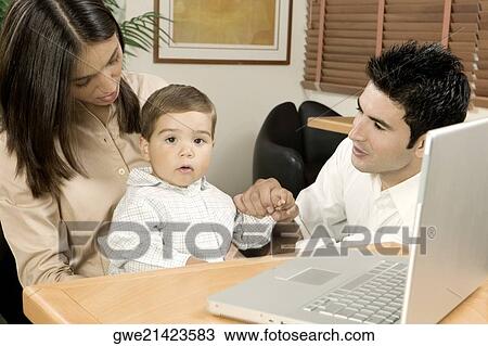 Stock Image - Portrait of a baby boy sitting in front of a laptop with his parents. Fotosearch