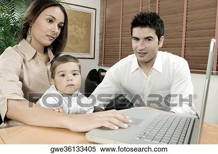 Stock Photography - Portrait of a baby boy sitting in front of a laptop with his parents. Fotosearch