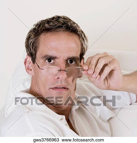 Stock Image - Portrait of a mid adult man adjusting his eyeglasses. Fotosearch