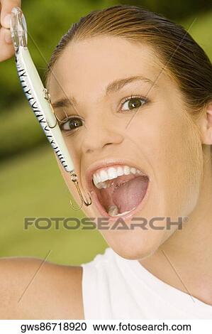 Stock Image - Portrait of a teenage girl holding a fishing lure near her mouth. Fotosearch