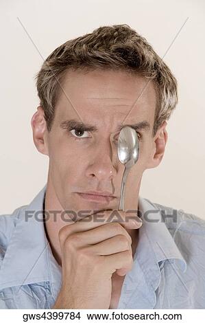 Portrait of a young man covering his eye with a spoon View Large Photo Image Picture - Portrait of a young man covering his eye with a spoon. Fotosearch