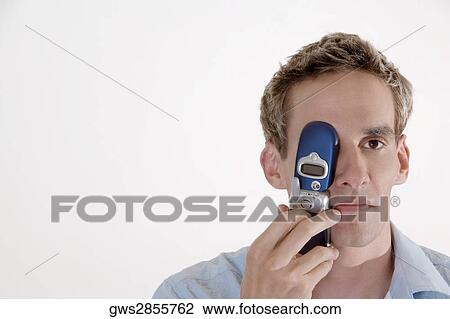 Portrait of a young man covering his eye with a mobile phone View Large Photo Image Stock Image - Portrait of a young man covering his eye with a mobile phone. Fotosearch