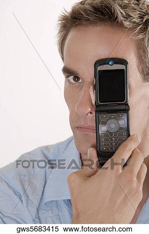 Portrait of a young man covering his eye with a mobile phone View Large Photo Image Stock Photography - Portrait of a young man covering his eye with a mobile phone. Fotosearch