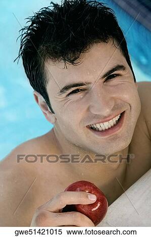 Stock Photography - Portrait of a young man holding an apple in a swimming pool. Fotosearch