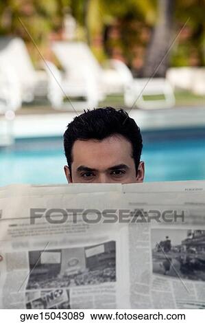 Stock Photo - Portrait of a young man peeping over a newspaper. Fotosearch