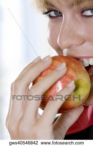 Stock Image - Portrait of a young woman biting an apple. Fotosearch