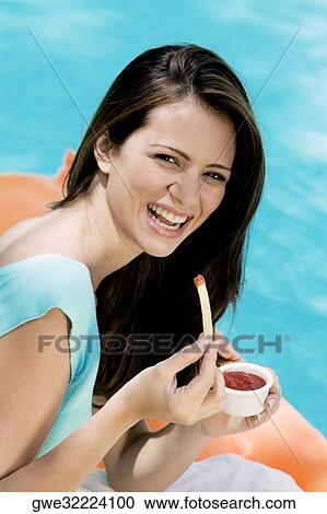 Stock Image - Portrait of a young woman eating french fries. Fotosearch