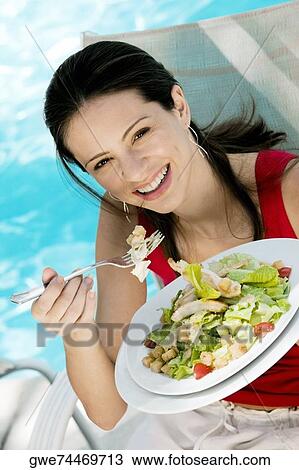 Stock Image - Portrait of a young woman eating salad. Fotosearch
