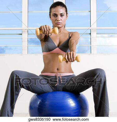 Stock Image - Portrait of a young woman exercising with dumbbells on a fitness ball. Fotosearch