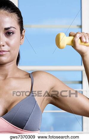 Portrait of a young woman exercising with a dumbbell View Large Photo Image Stock Photo - Portrait of a young woman exercising with a dumbbell. Fotosearch